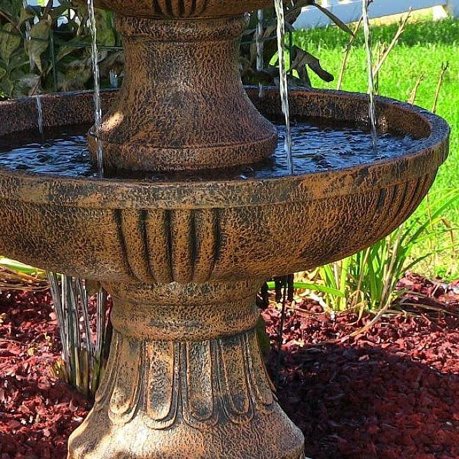 A água escorre suavemente da torneira para uma pequena piscina no fundo da fonte